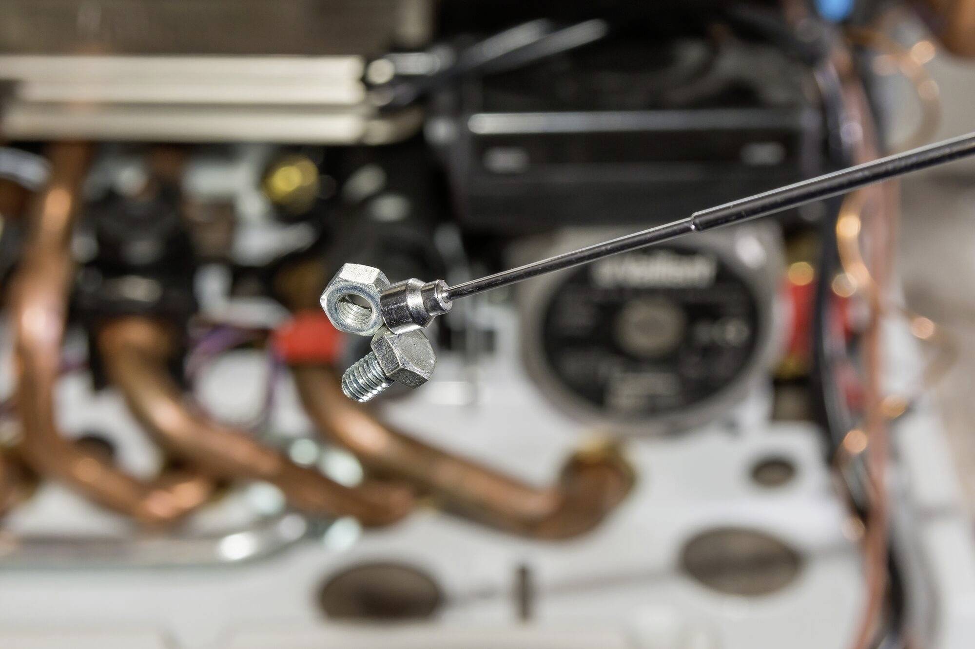 Nahaufnahme eines magnetischen Greifers hält Muttern und Schrauben vor einem unscharfen Hintergrund aus Kupferrohren und Maschinenteilen.