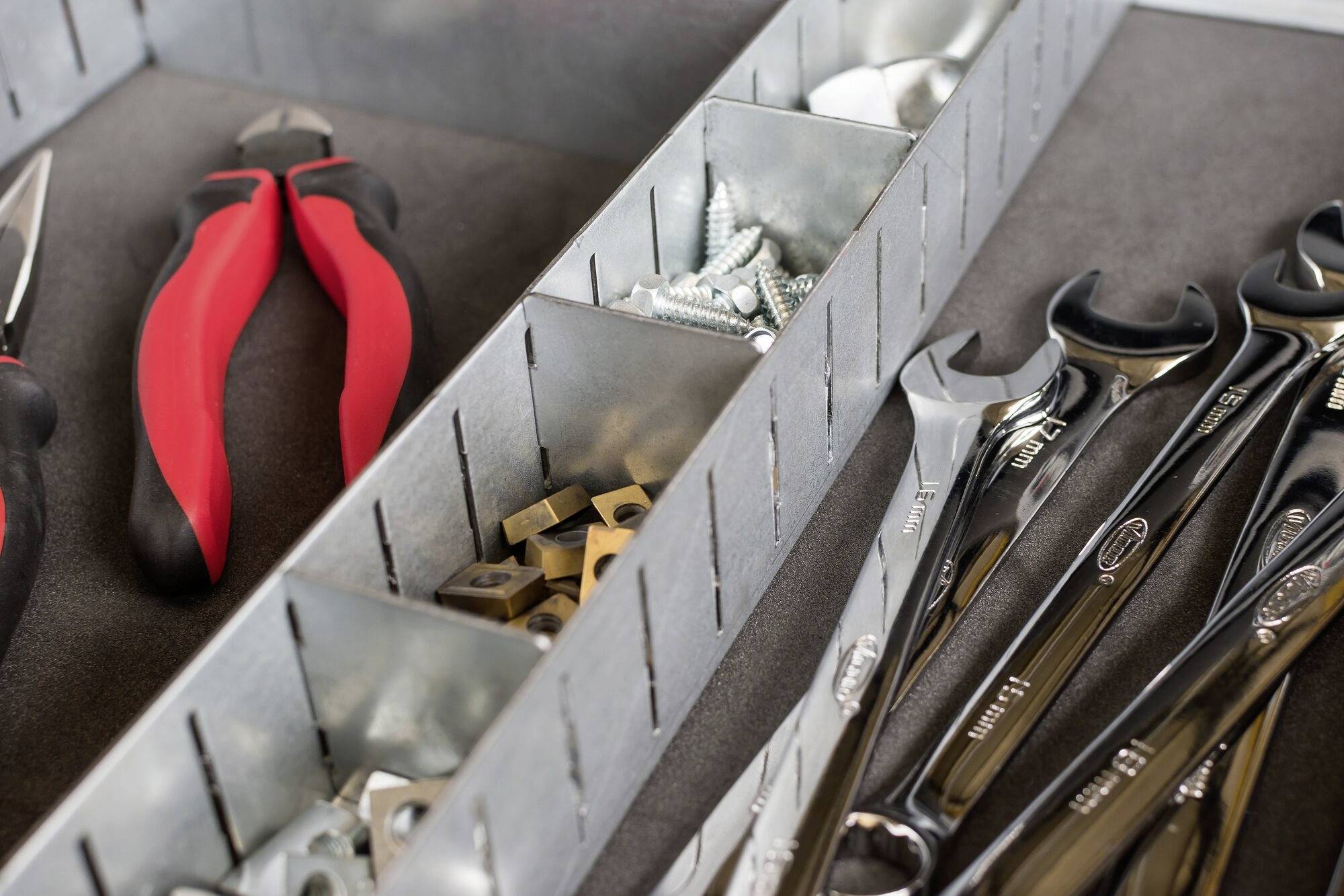 Ein geöffneter Werkzeugkasten mit roten Zangen, Schrauben, Muttern und verschiedenen Schraubenschlüsseln.