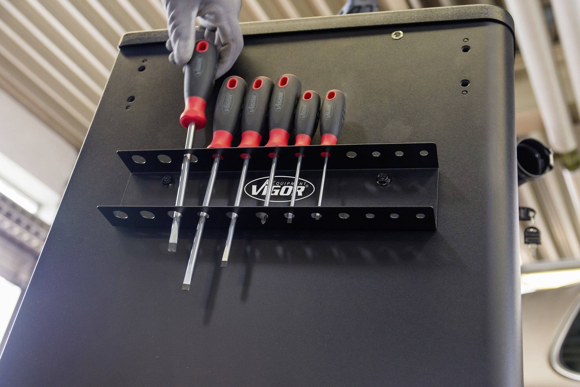 Eine Hand platziert einen Schraubenzieher in einen Halter, der an einem Werkzeugwagen befestigt ist. Der Halter ist mit mehreren Schraubenziehern bestückt.