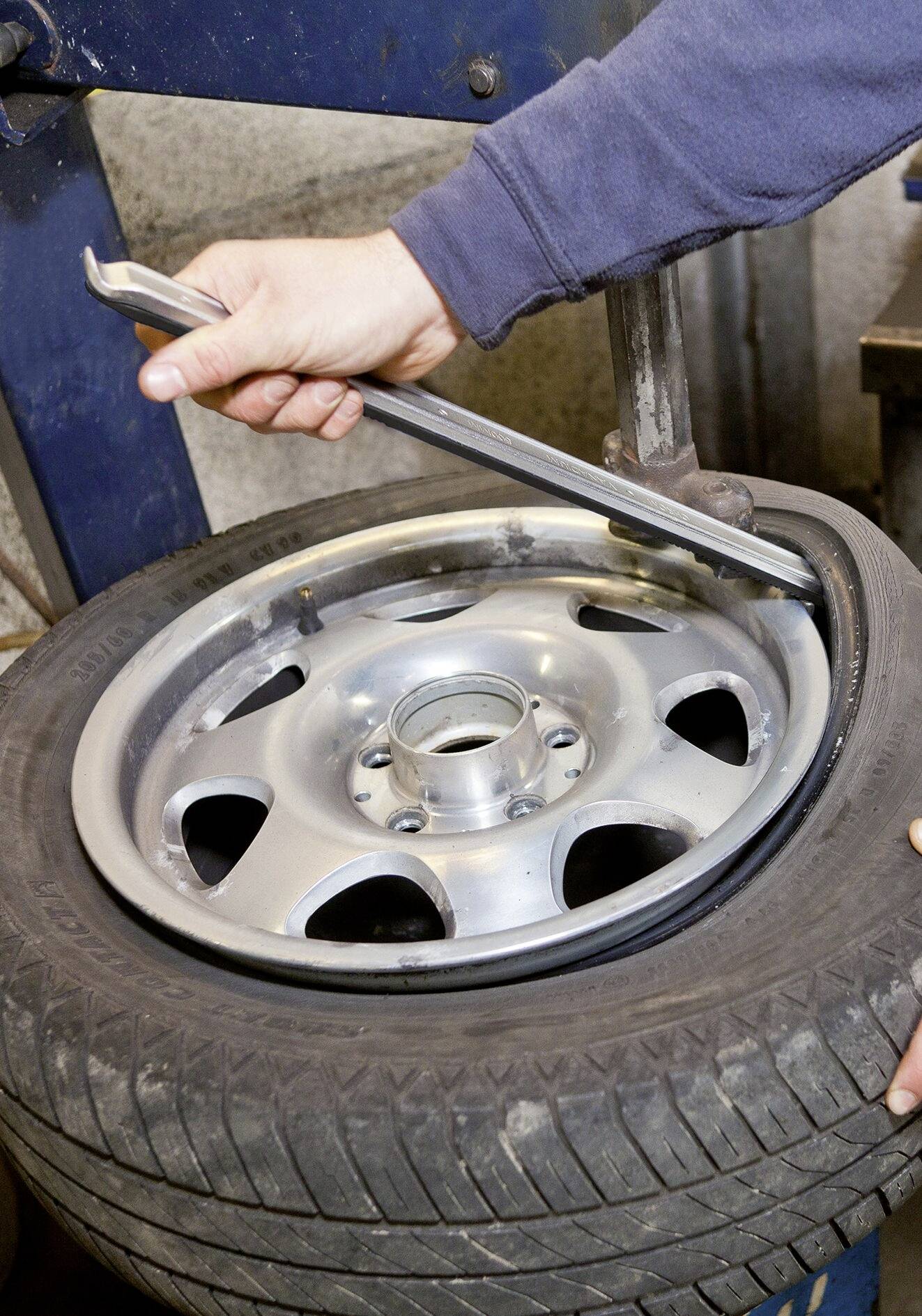 Eine Person montiert mit einem Hebelwerkzeug einen Autoreifen auf eine Felge in einer Werkstattumgebung.