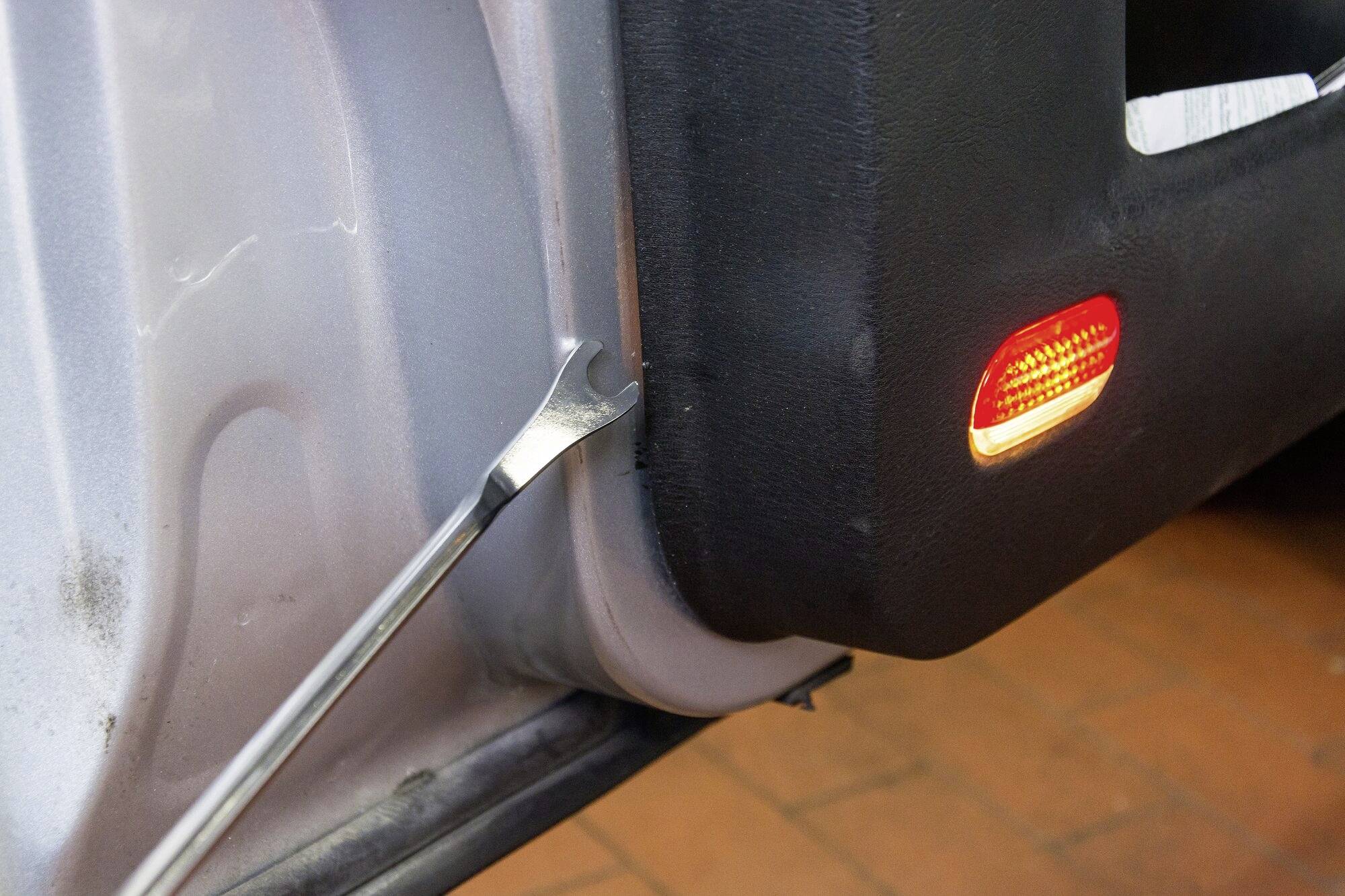Ein Reifenheber wird benutzt, um eine Autotürverkleidung zu entfernen. Ein Warnlicht ist an der Verkleidung zu sehen.