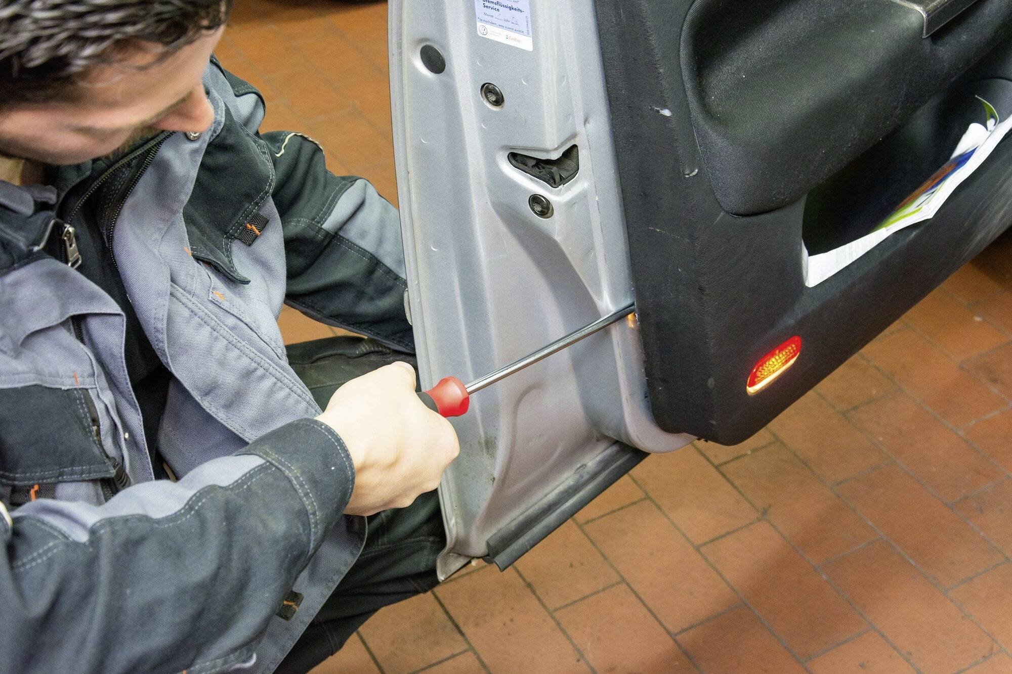 Ein Mechaniker repariert die Innenseite einer Autotür mit einem Schraubendreher in einer Werkstatt.