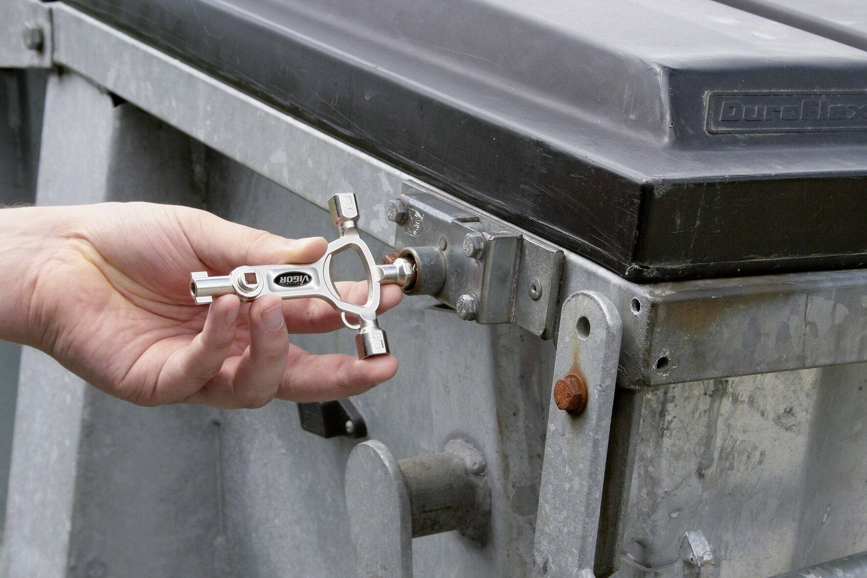 Eine Hand dreht mit einem Vierkantschlüssel die Schlossverriegelung eines verschlossenen Metallcontainers auf.