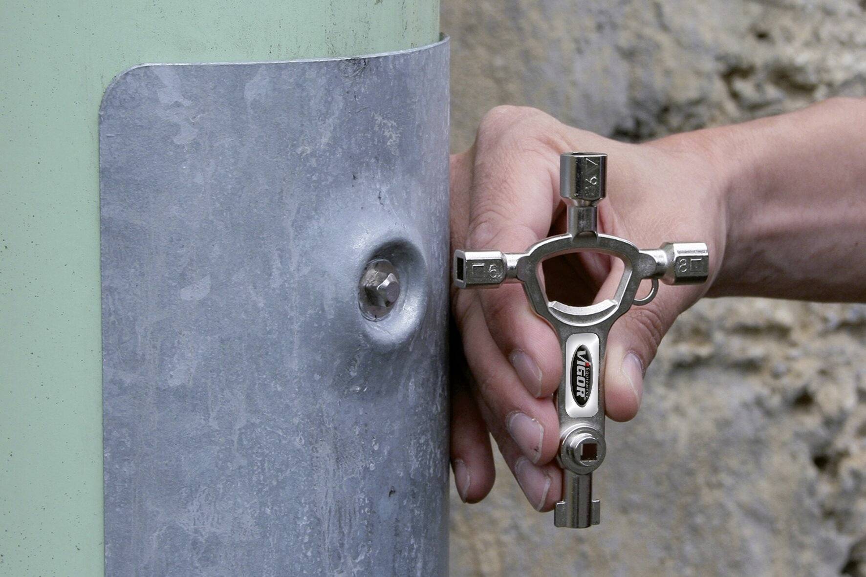 Eine Hand verwendet ein Werkzeug mit mehreren Schlüsselformen, um eine Schraube an einer Metallplatte zu öffnen.