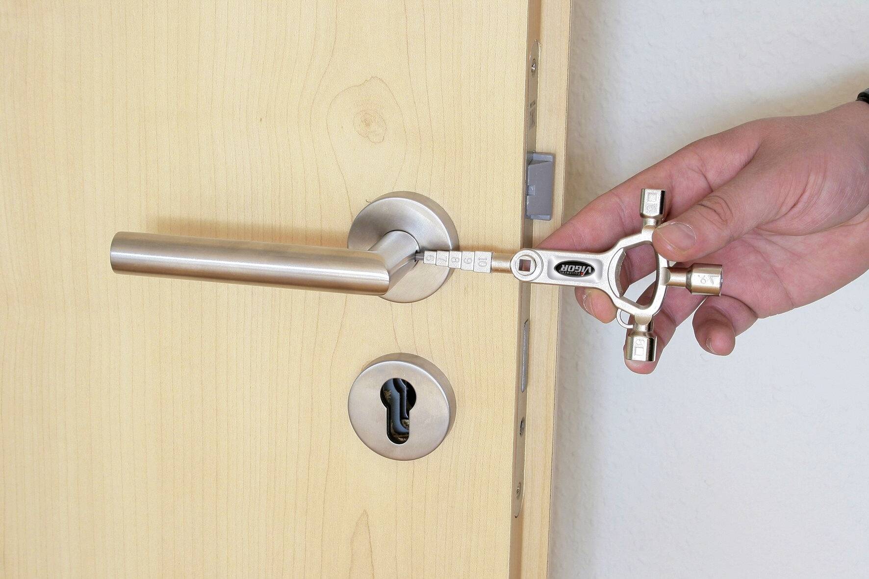 Eine Hand hält einen Vierkantschlüssel und steckt ihn in eine Tür mit einem silbernen Griff, um sie zu entriegeln.