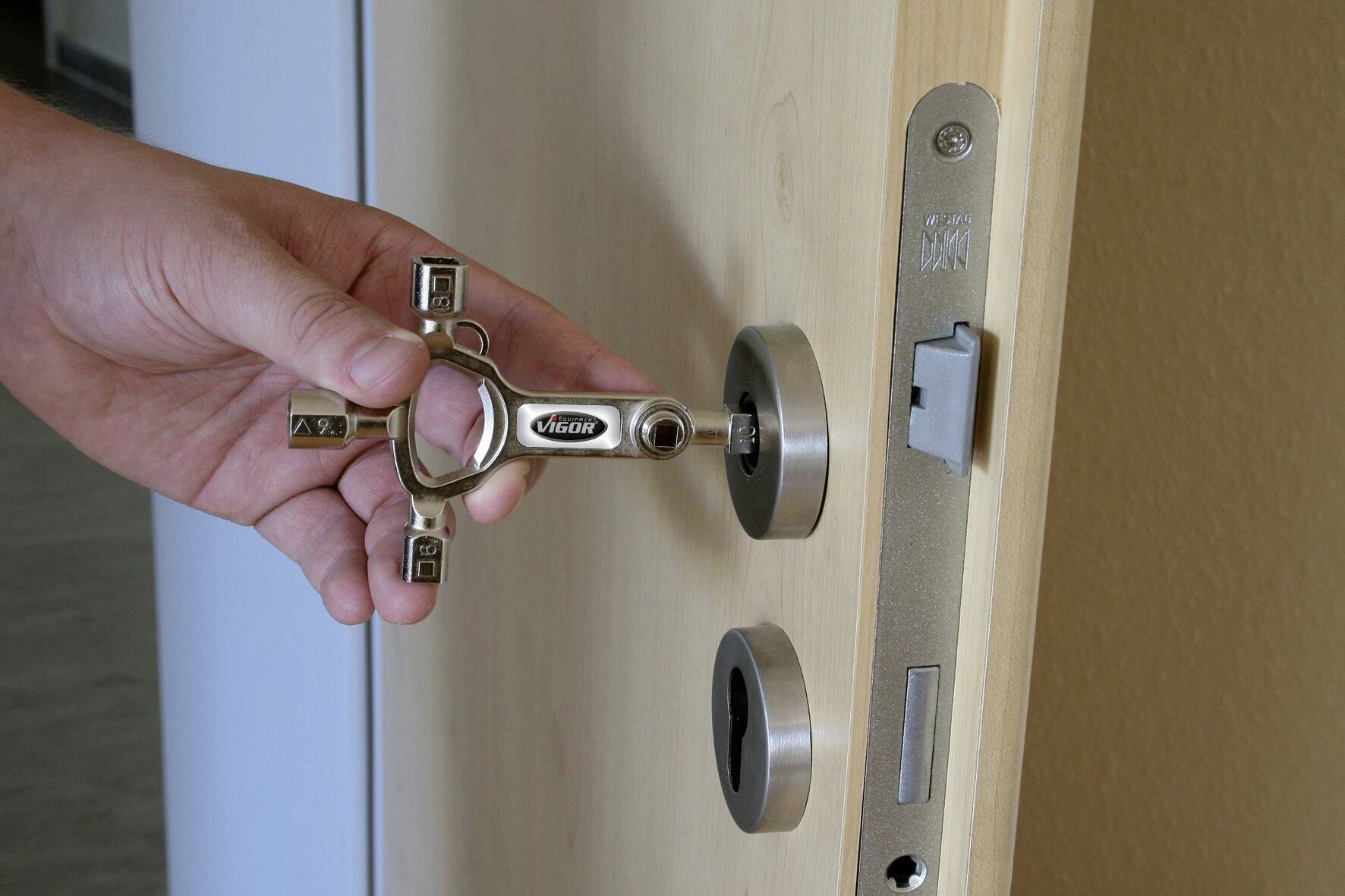 Eine Hand steckt einen Sicherheitsschlüssel in ein Türschloss. Die Tür ist aus hellem Holz, und der Raum dahinter ist teilweise sichtbar.