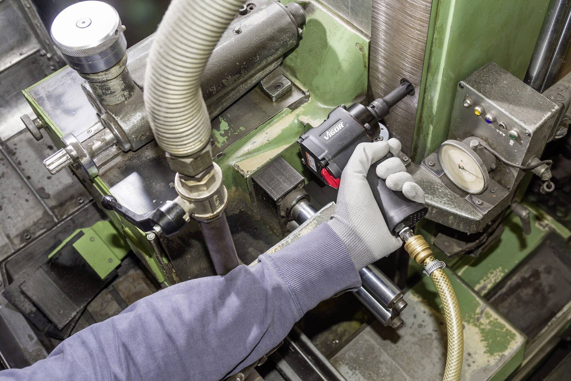 Eine Person bedient eine industrielle Schleifmaschine, um ein Metallwerkstück zu bearbeiten. Ein Messgerät zeigt den Druck an.