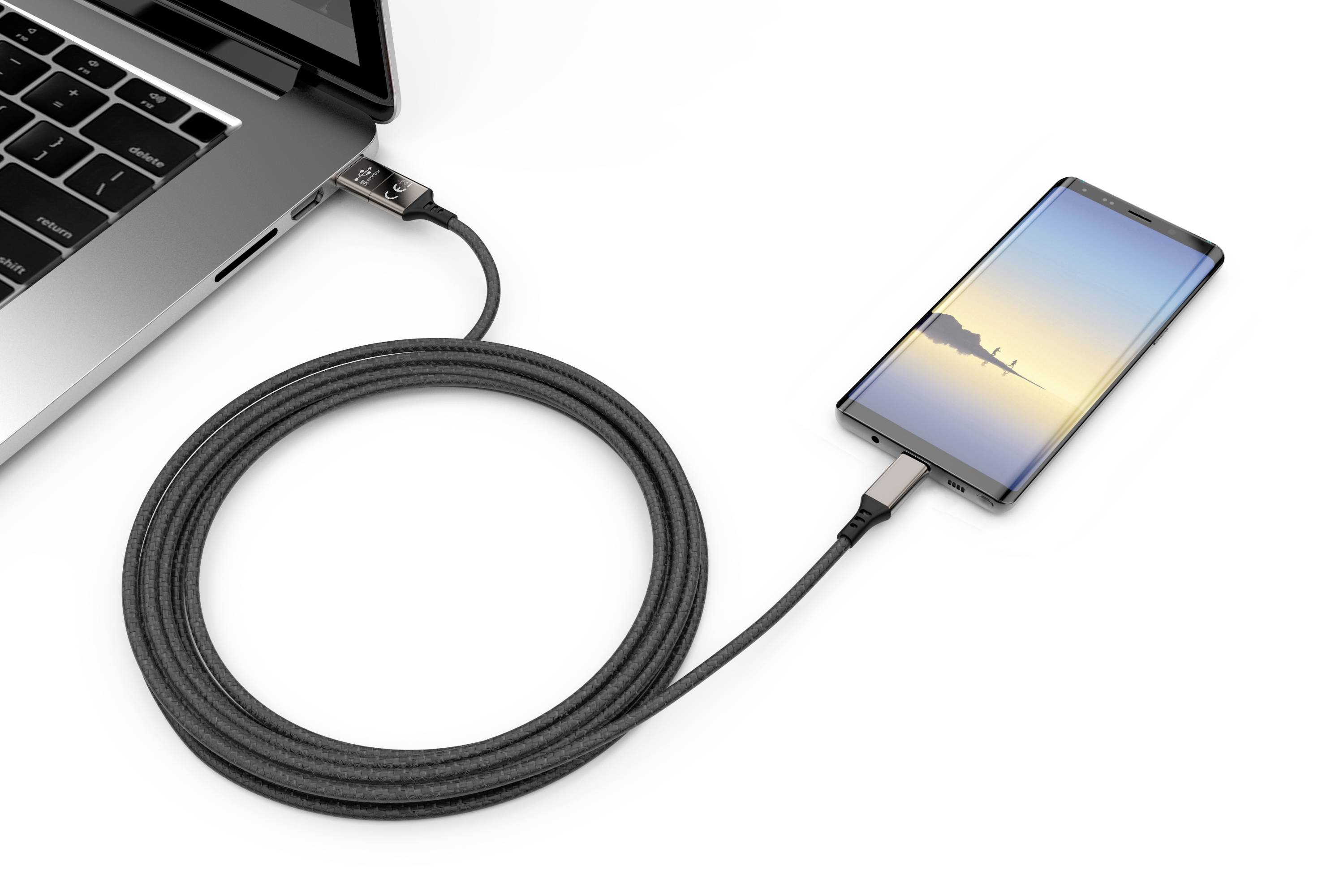 Smartphone lädt über ein Kabel an einem Laptop. Das Smartphone zeigt einen Sonnenuntergangshintergrund.