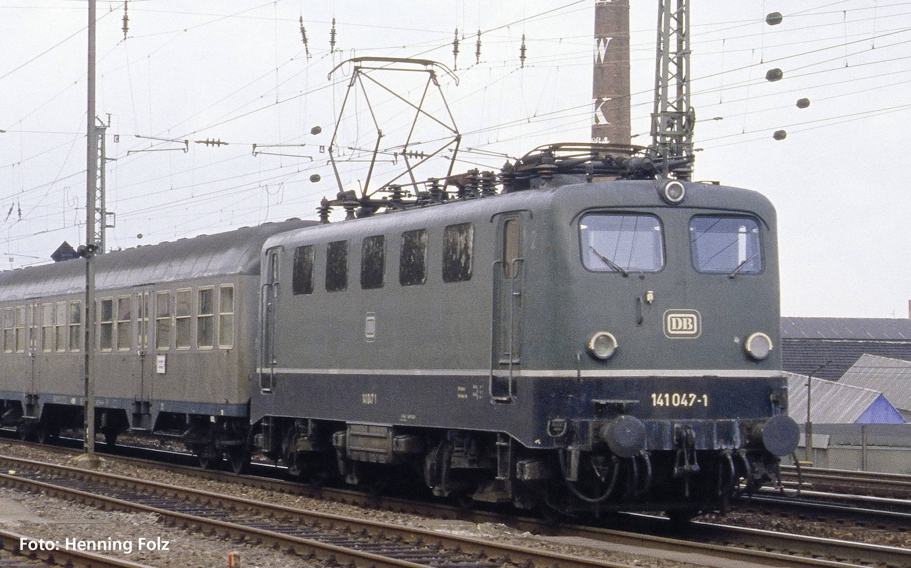 Ein oldtimergrüner deutscher E-Lok-Zug fährt auf Schienen, gezogen von einer Lokomotive mit der Nummer 141 047-1, an Oberleitungen vorbei.