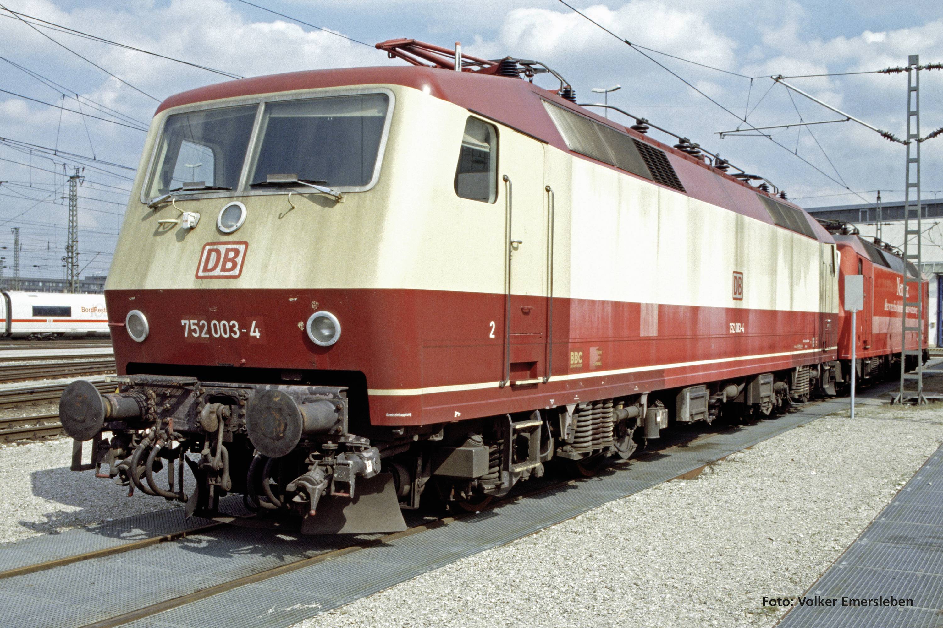 Eine beige-rote Elektrolokomotive der Deutschen Bahn steht auf einem Gleis. Links ist ein weiterer Zug im Hintergrund sichtbar.