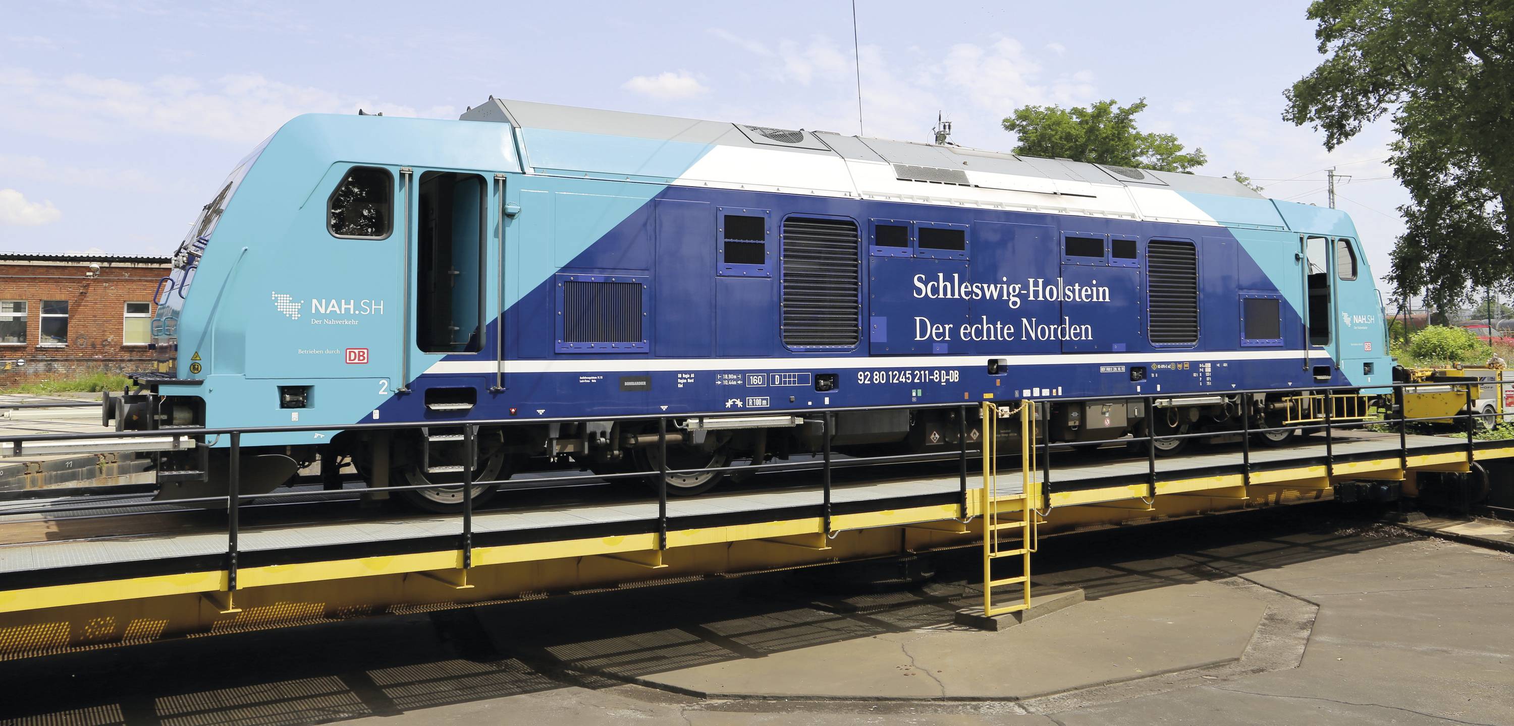 Eine blaue Lokomotive mit der Aufschrift 'Schleswig-Holstein Der echte Norden' steht auf einer Drehscheibe im Freien.