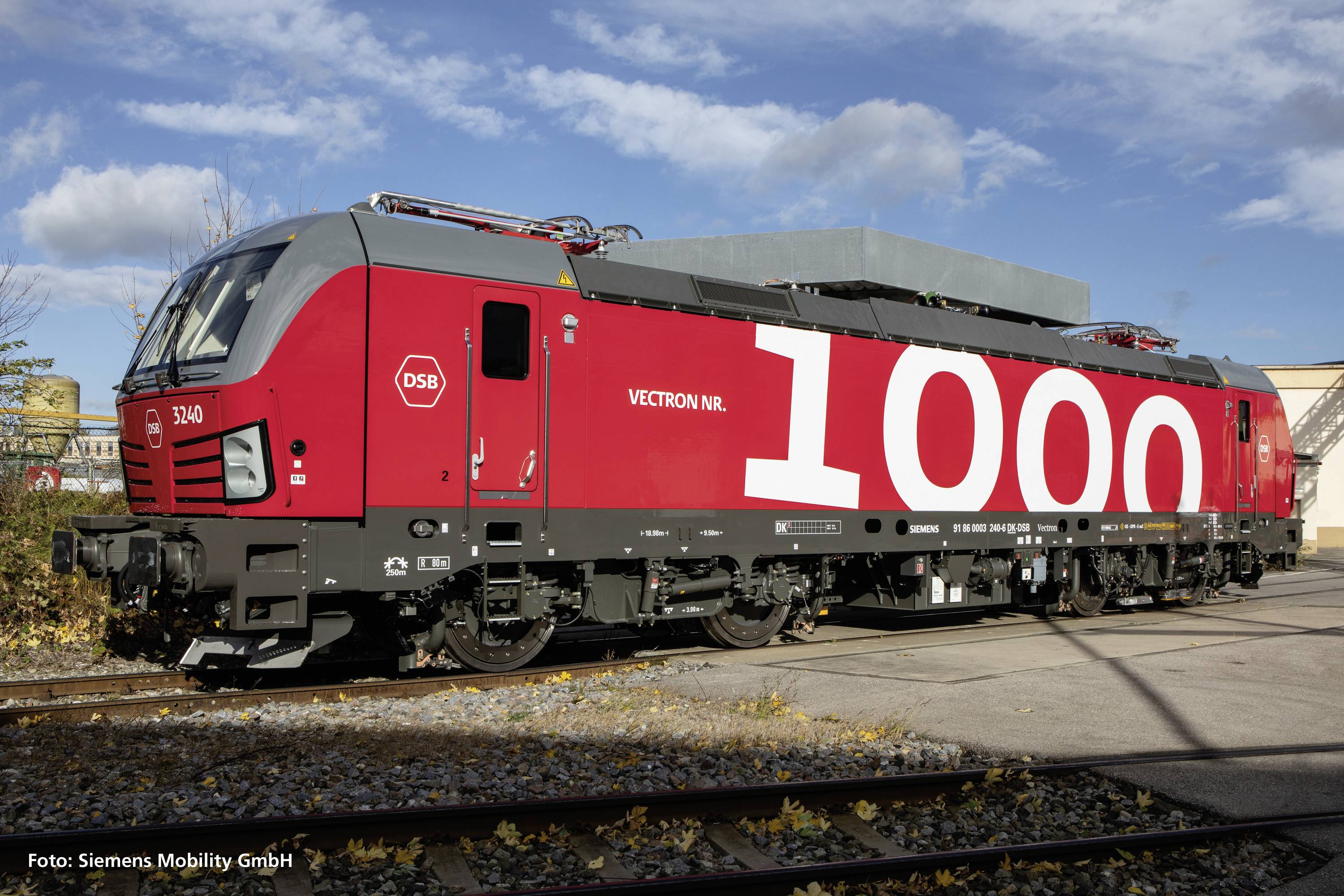 Roter Zug mit der Aufschrift '1000' auf der Seite, fotografiert bei Sonnenschein auf einem Industriegleis.