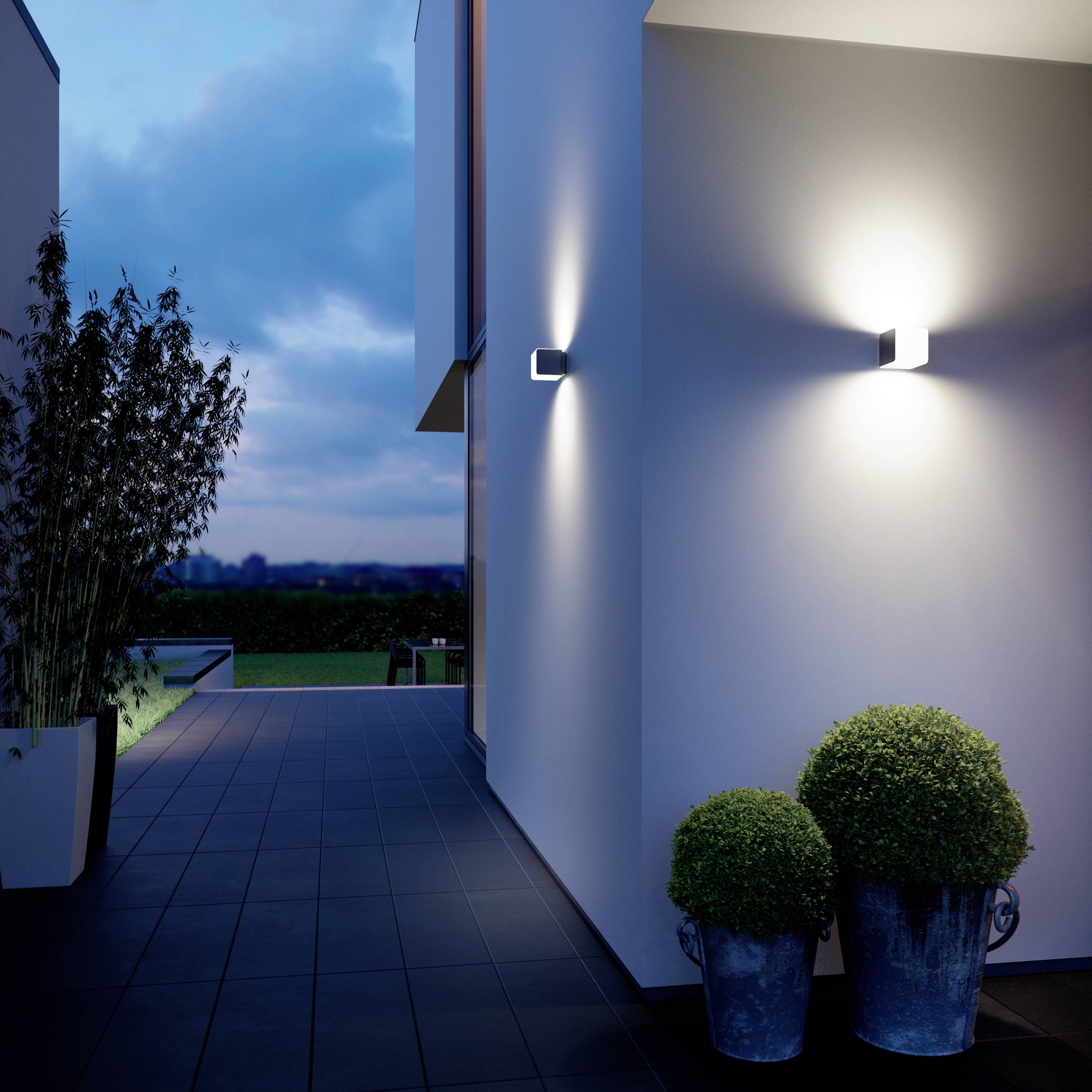 Moderne Hausfassade am Abend mit eingelassenen Wandlampen, die warmes Licht verbreiten. Im Vordergrund eine dekorative Pflanze.