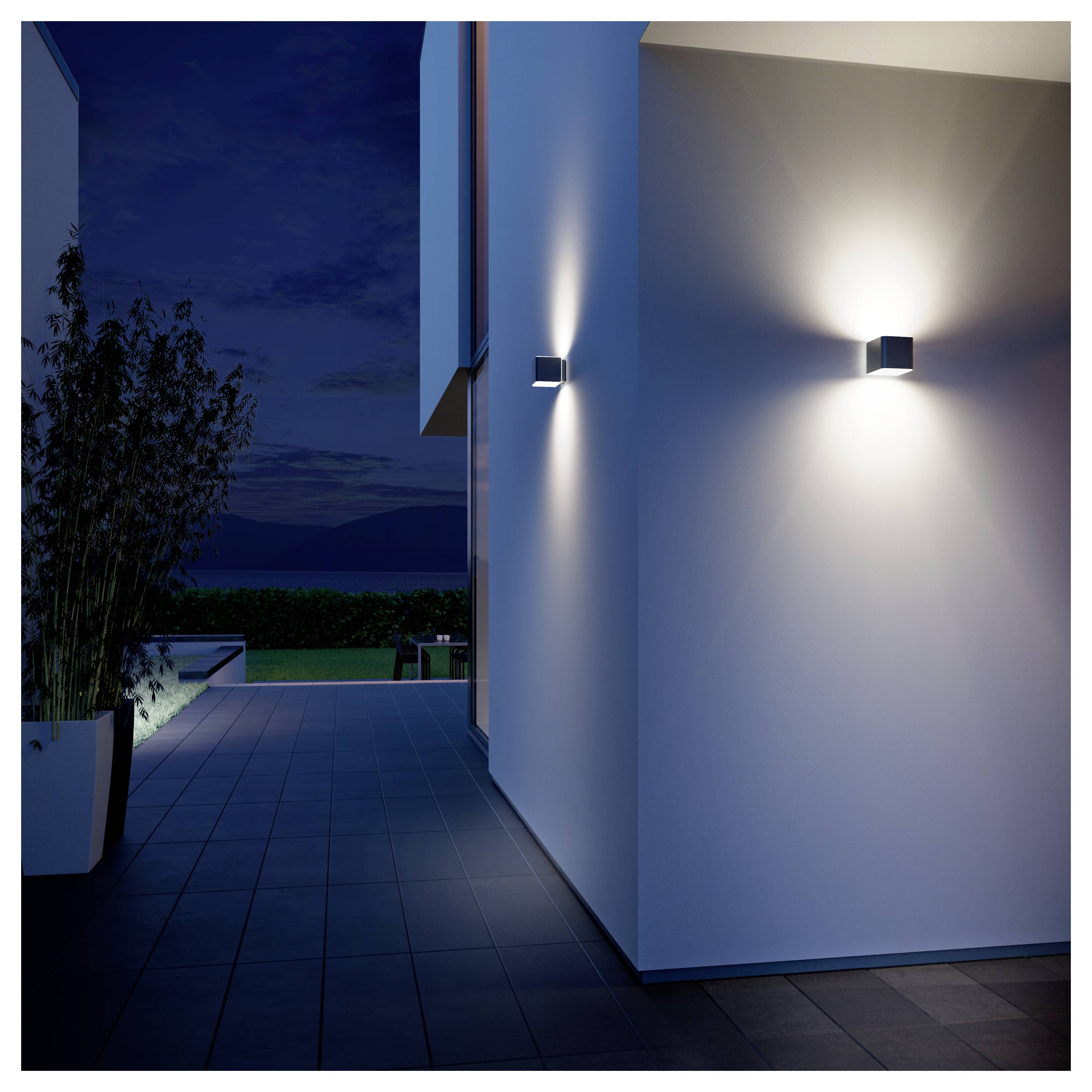 Modernes Hausäußeres in der Nacht mit wandmontierten Leuchten, die eine weiße Fassade und einen gefliesten Gehweg neben einer Topfpflanze beleuchten.