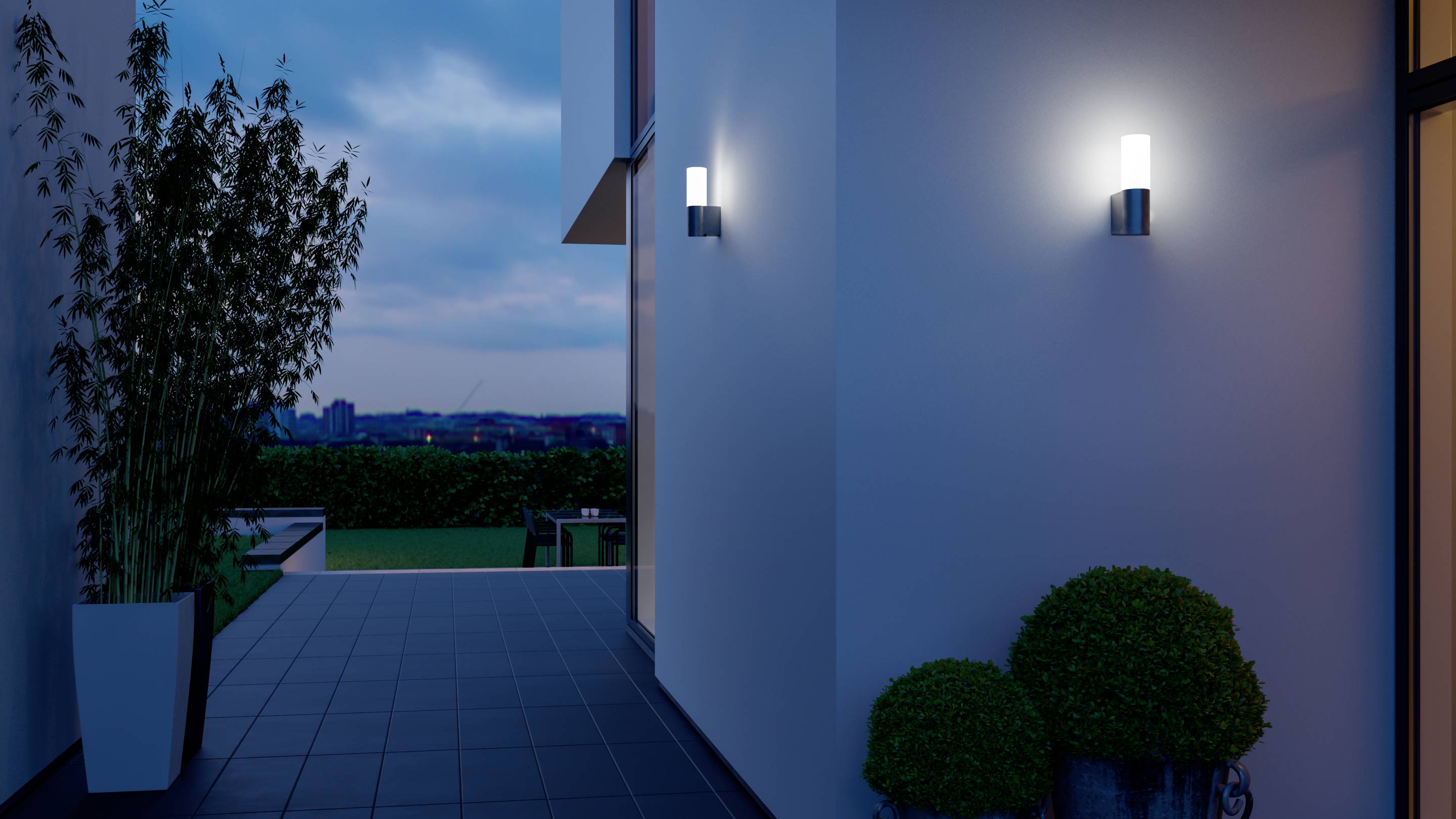 Außenbereich eines modernen Hauses bei Dämmerung, mit leuchtender Wandlampe und Topfpflanzen neben einem Gehweg.
