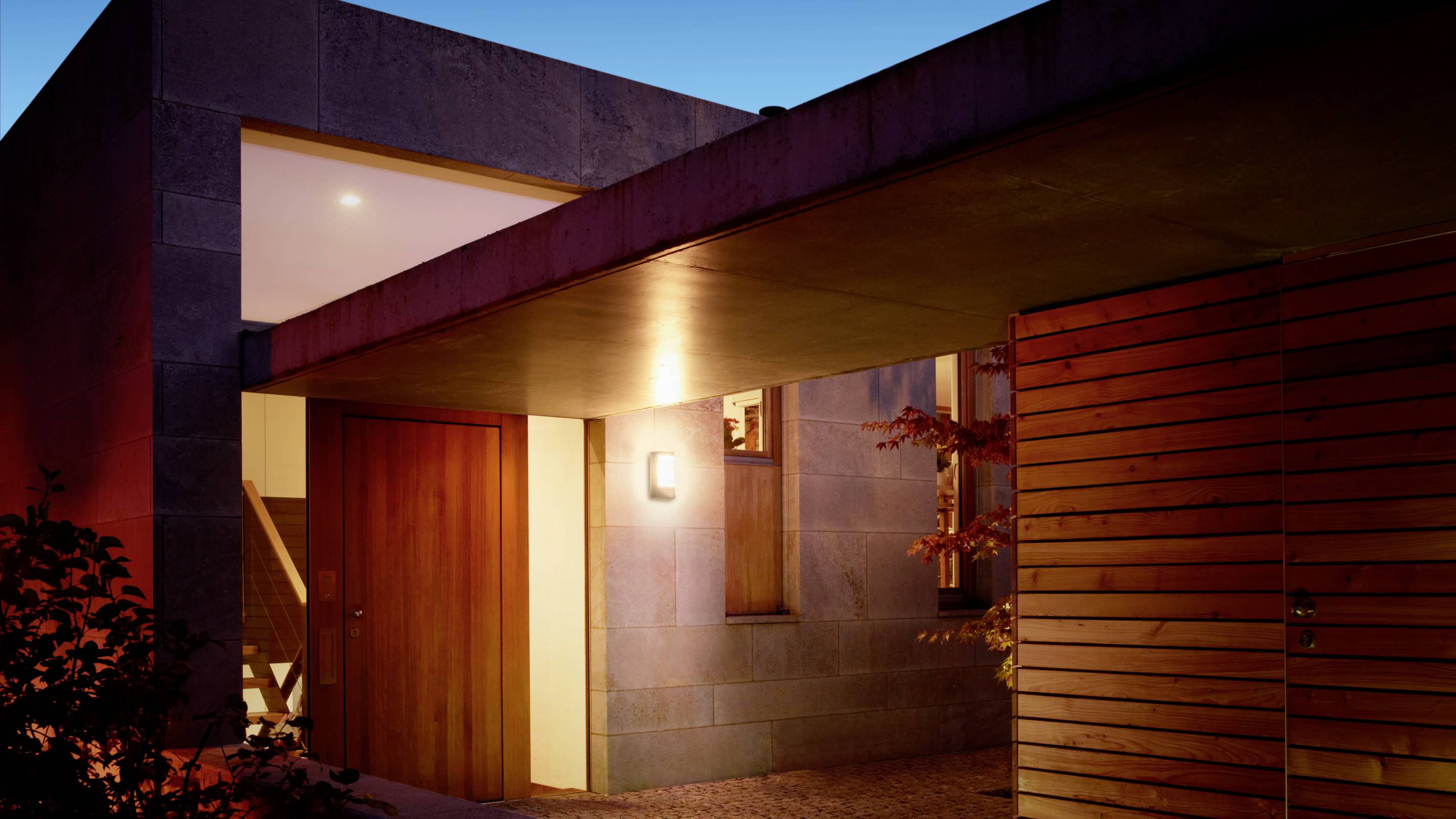 Ein modernes Haus bei Nacht, beleuchtet von Außenlampen. Holz- und Steinmaterialien dominieren die Architektur.