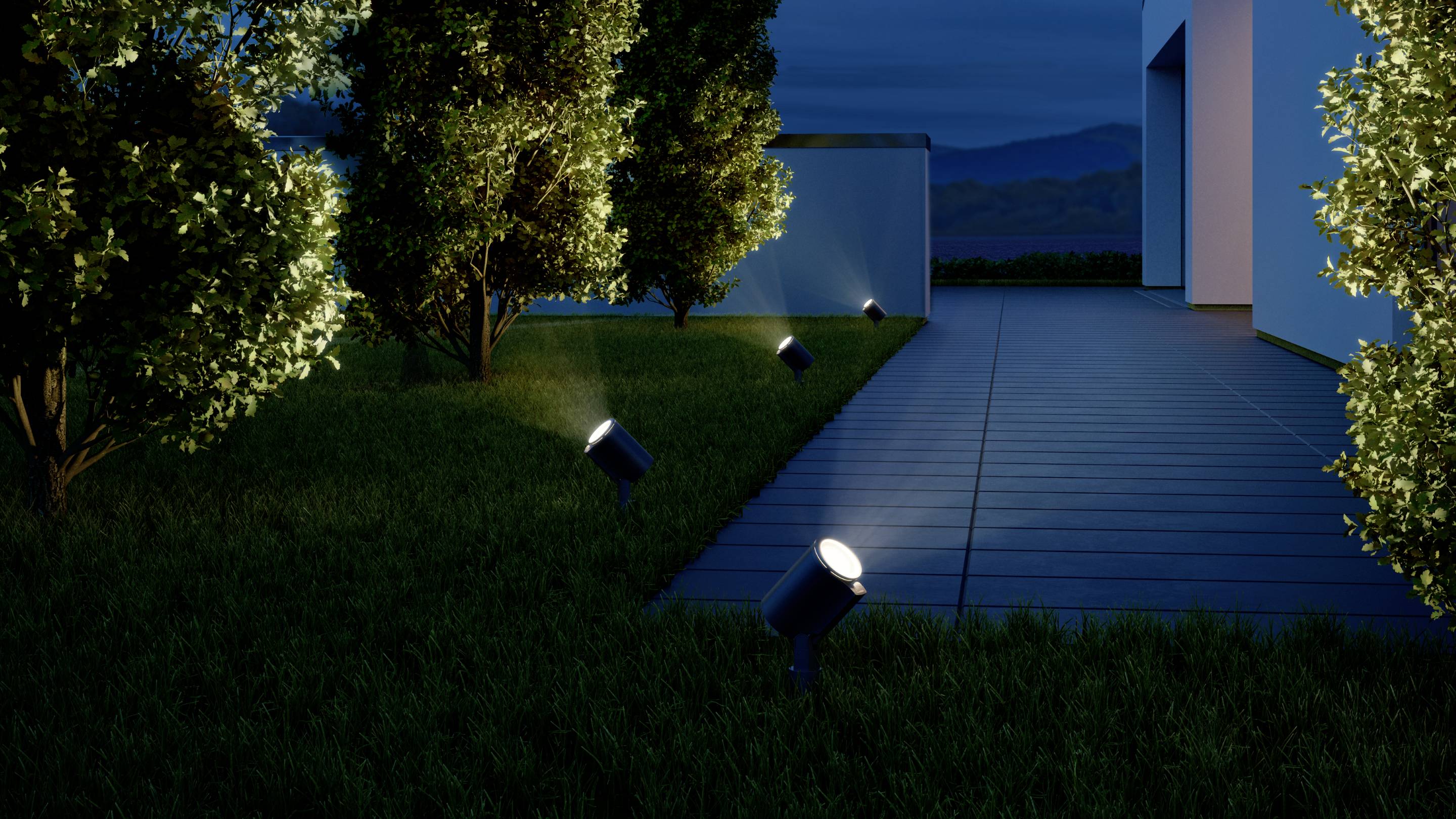 Ein Weg am Haus wird bei Nacht von mehreren kleinen Gartenlichtern erleuchtet. Bäume umrahmen den Weg und sind leicht beleuchtet.