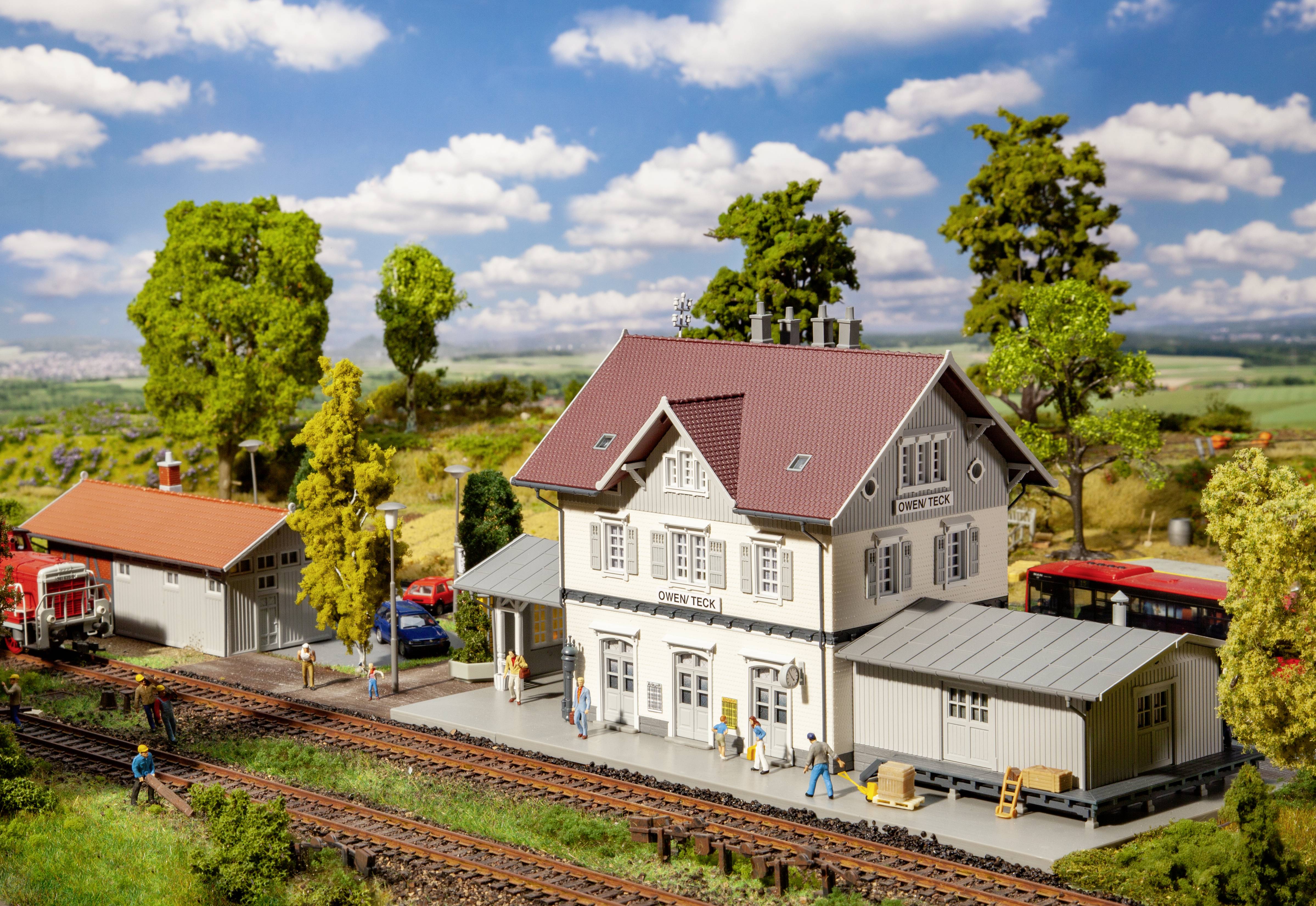 Miniatur-Modell eines Bahnhofs mit einem Hauptgebäude, Nebengebäude und Bahnsteigen. Bäume und Wiesen umgeben das Ensemble.