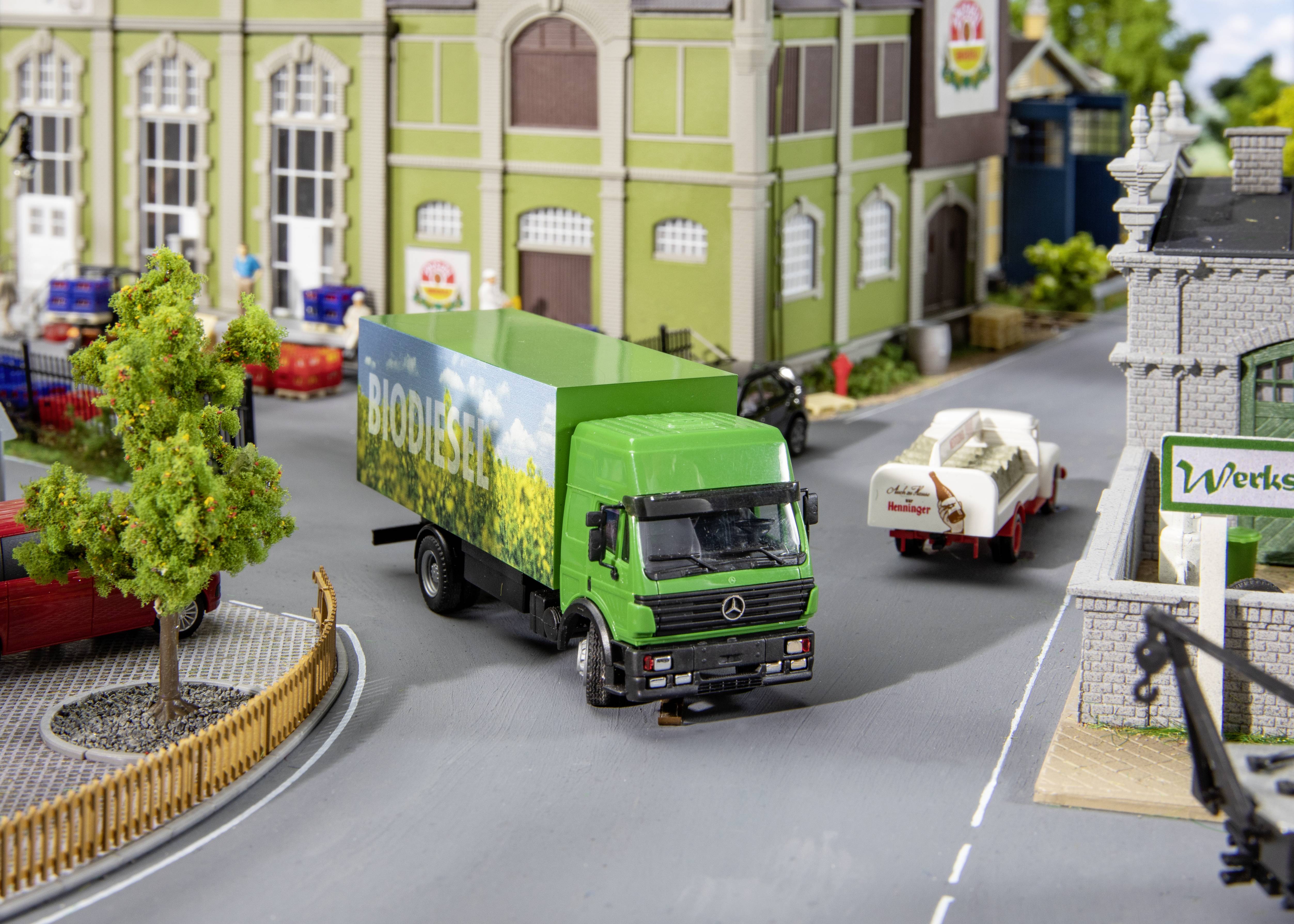 Ein grüner Lastwagen mit der Aufschrift 'Biodiesel' fährt durch eine Miniaturstadt mit Gebäuden und geparkten Autos.