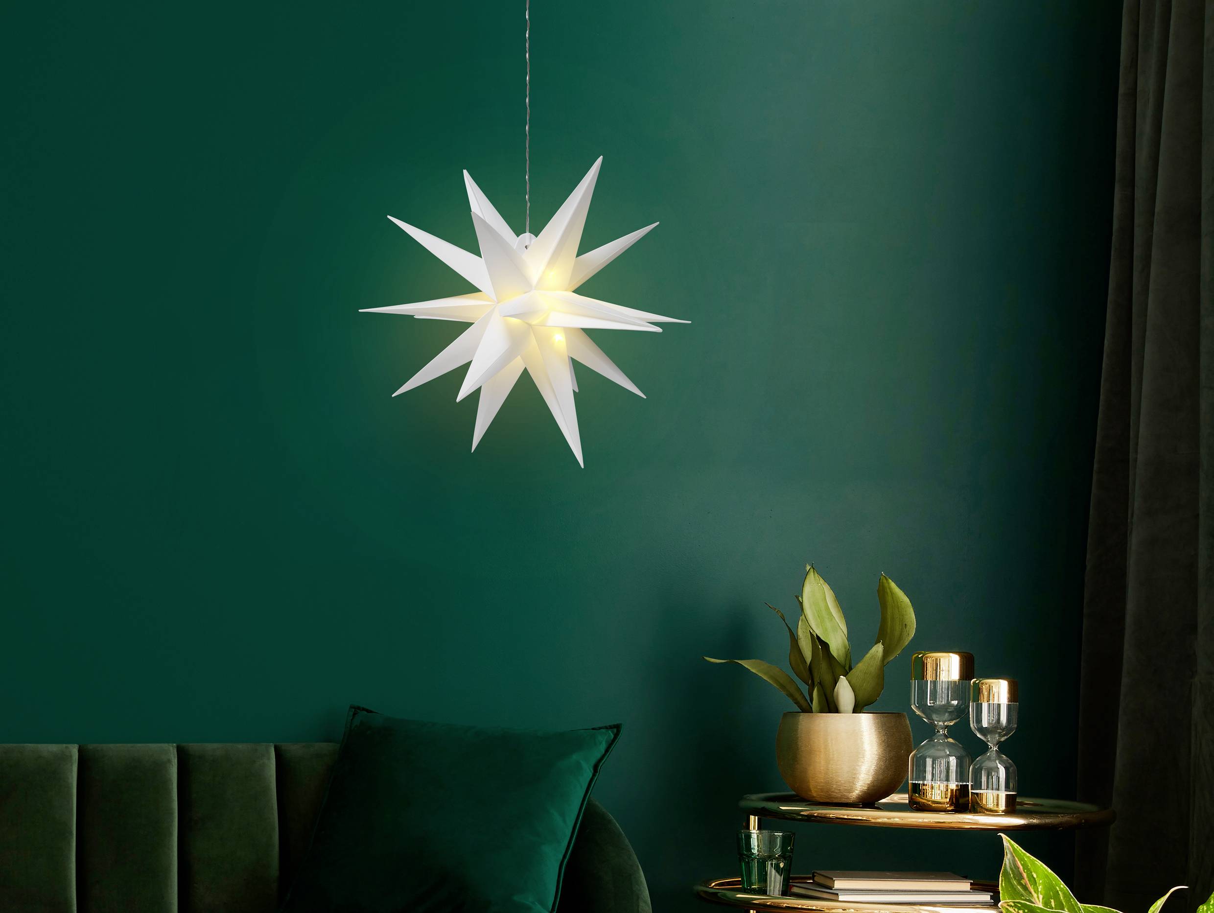 Weihnachtsstern-Laterne leuchtet an der Decke in einem Raum mit grüner Wand, grünem Sofa und topfgepflanzten Pflanzen auf einem Tisch.