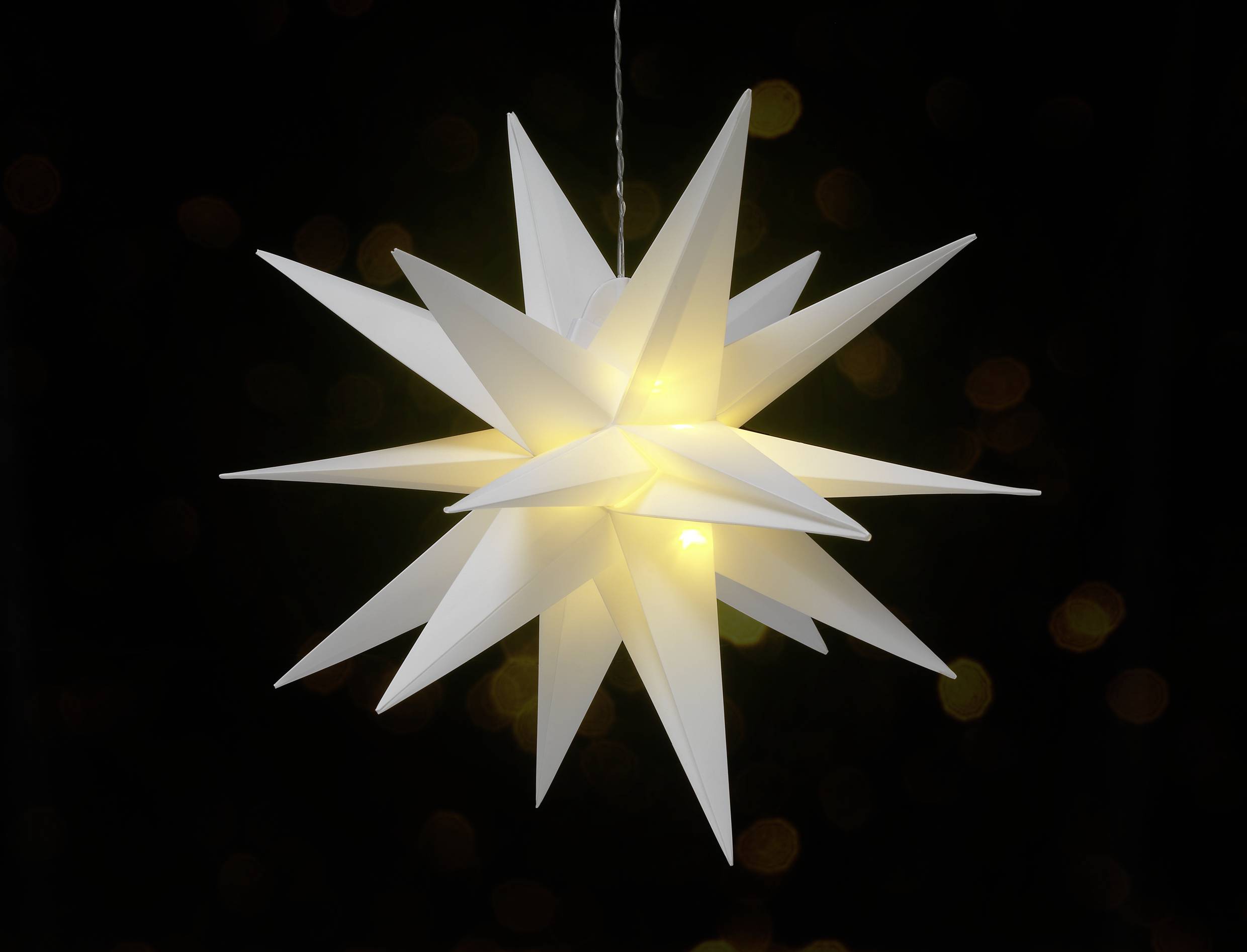 Weißer Papierstern mit strahlendem Licht in der Mitte, vor einem dunklen Hintergrund.
