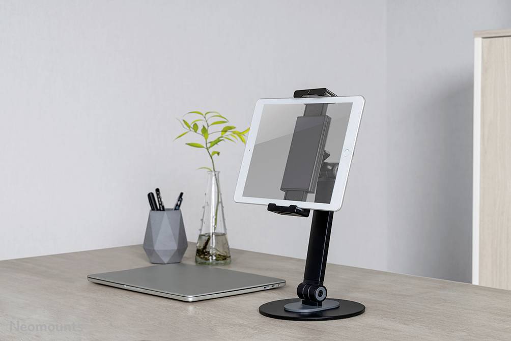 Schreibtisch mit Laptop, Tablet-Halterung und Vase mit Pflanze, moderner und aufgeräumter Arbeitsbereich.