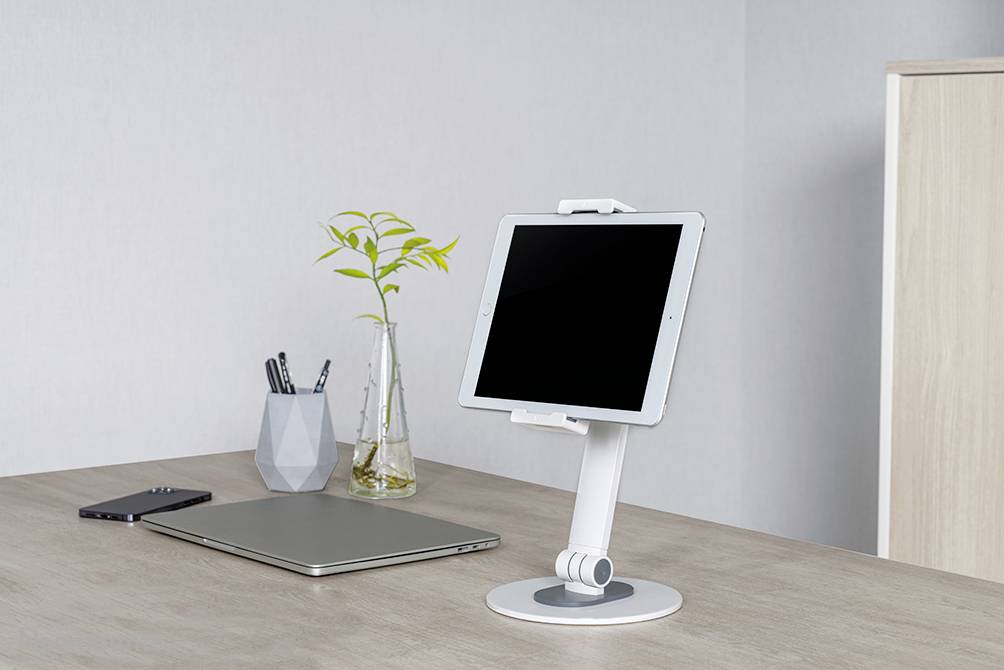 Ein Schreibtisch mit einem Tablet auf einem Ständer, einem Laptop, einem Smartphone und einem Stiftehalter mit Pflanzenverzierung.