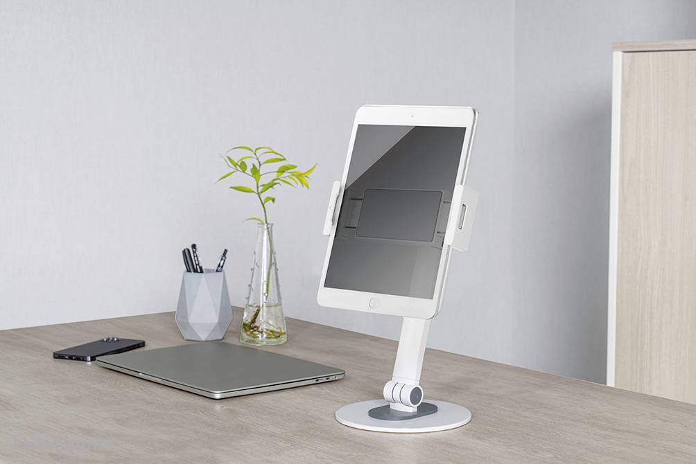Tablet-Halterung auf minimalistischem Schreibtisch mit Laptop, Smartphone, Stiftehalter und Pflanze.