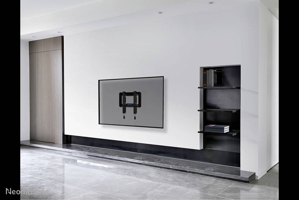 Flachbildfernseher an einer modernen weißen Wand montiert, linke Seite mit Holzpaneel, rechter eingebauter Regalbereich mit Büchern.