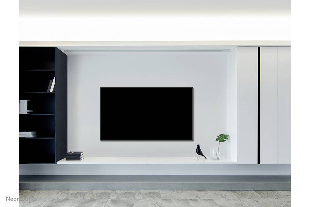 Ein modernes Wohnzimmer mit einem großen, schwarzen Fernseher an der Wand. Rechts ein Vogel-Designobjekt und eine Vase mit Pflanzen.