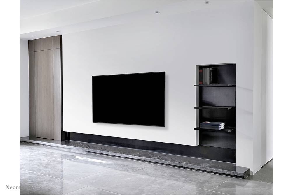 Ein modernes Wohnzimmer mit einem großen, schwarzen Flachbildfernseher an einer weißen Wand, daneben ein Regal mit Büchern.