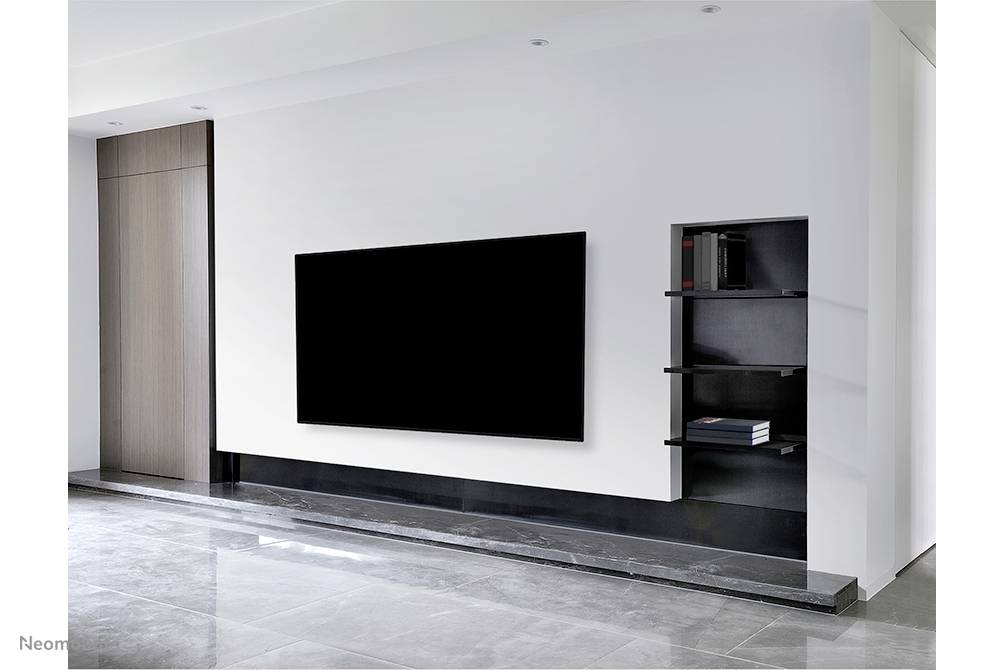 Ein modernes Wohnzimmer mit einem großen schwarzen Flachbildfernseher an einer weißen Wand. Rechts daneben ein Regal mit Büchern.