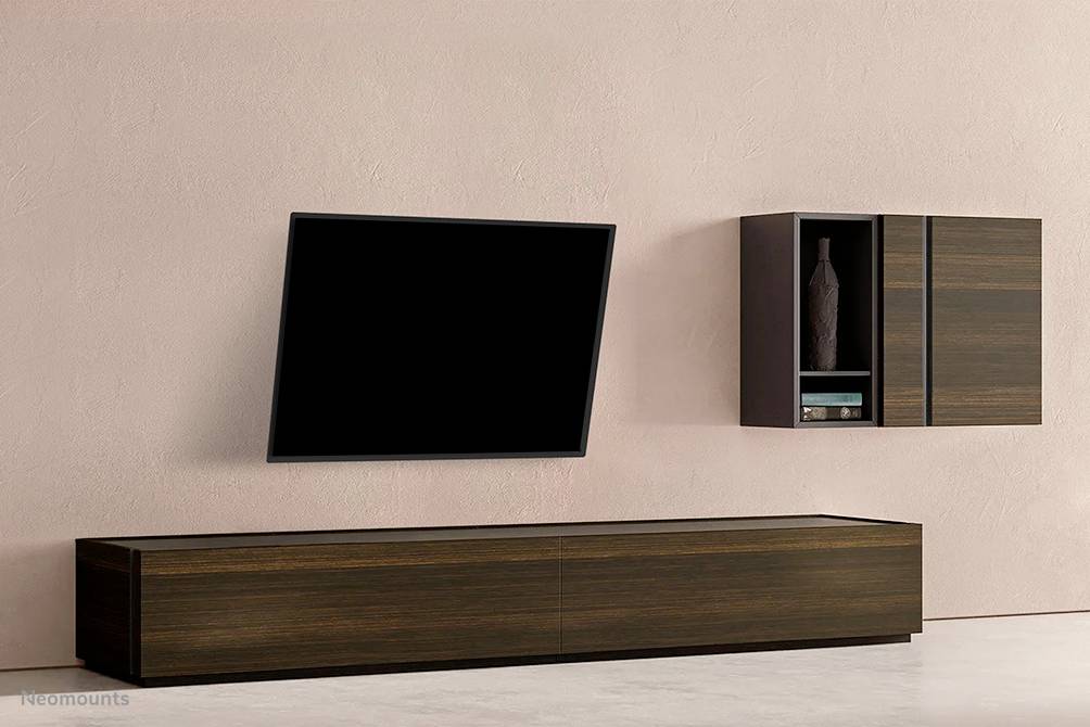 Ein modernes Wohnzimmer mit einem an der Wand montierten Fernseher, einem hölzernen TV-Schrank und einem Wandregal mit Vase.