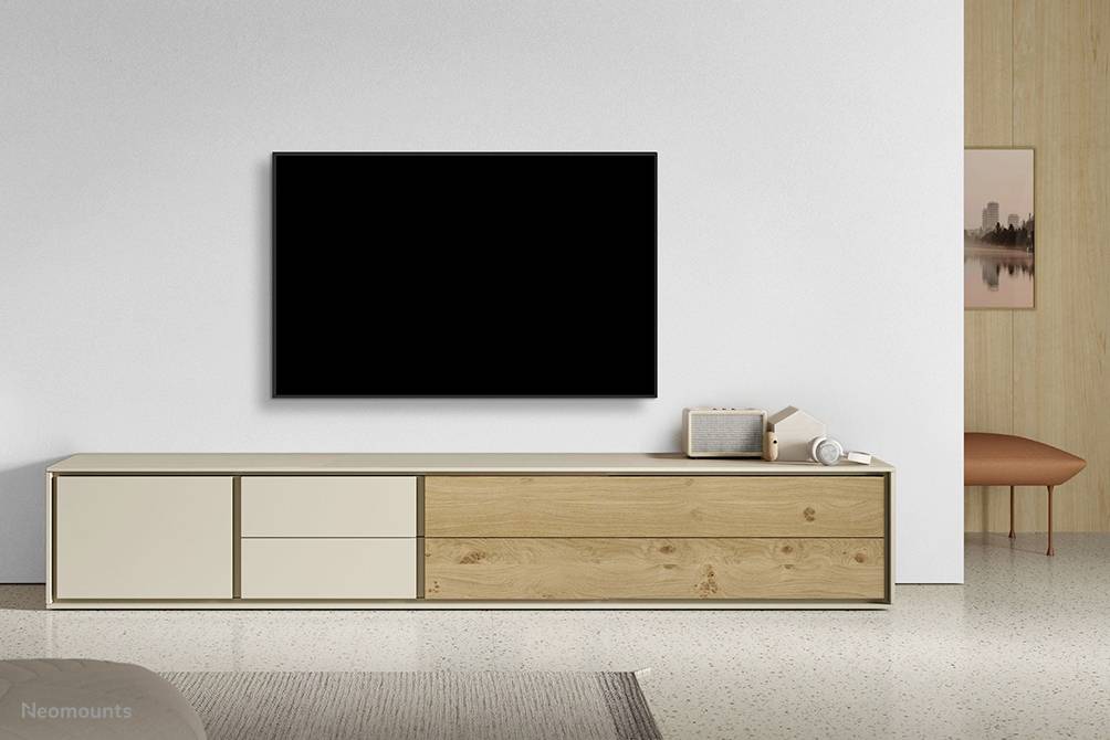 Ein minimalistisches Wohnzimmer mit einem großen Fernseher an der Wand. Darunter steht ein schlichtes Sideboard mit dekorativen Gegenständen.