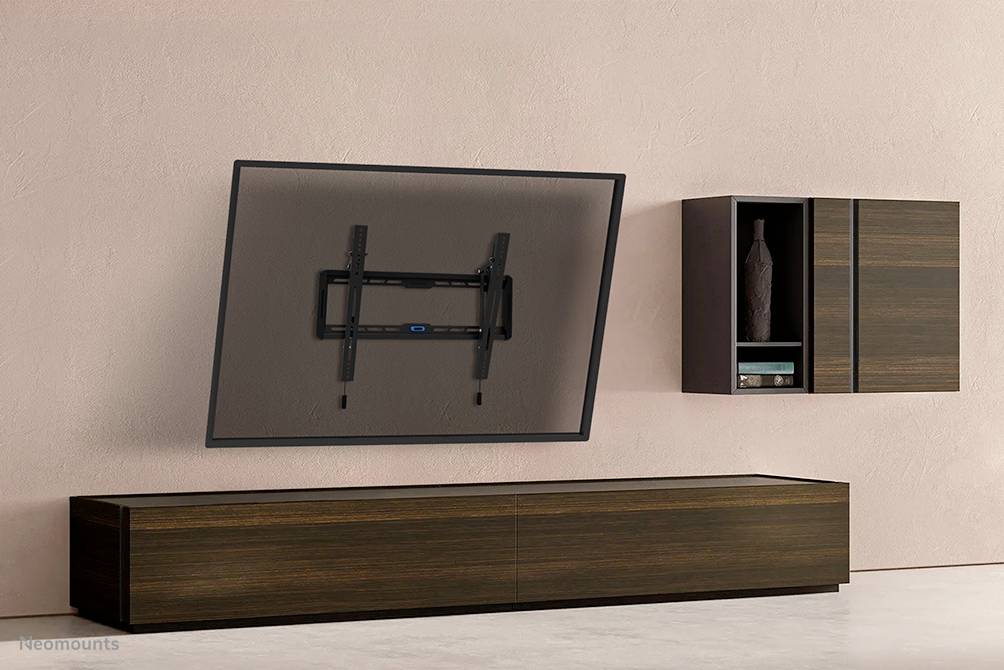 Wandmontage für TV an moderner rosa Wand, schwenkbar. Rechts daneben ein Holzschrank mit Vase. Darunter ein niedriges Holzsideboard.