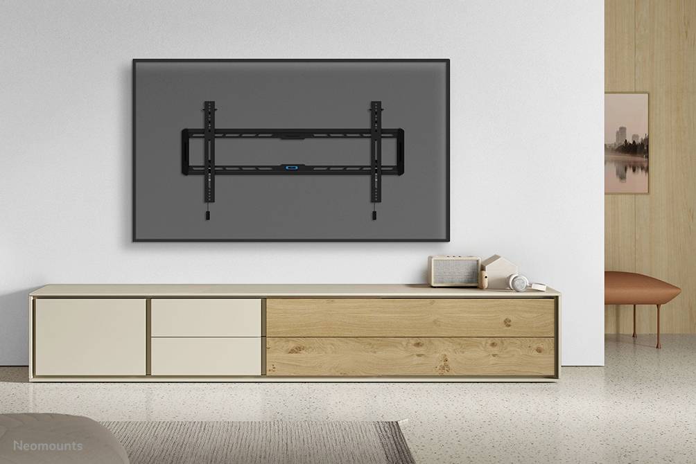 Ein Wohnzimmer mit einer modernen, schlichten Anrichte vor einer weißen Wand. An der Wand ist eine Halterung für einen Fernseher montiert.