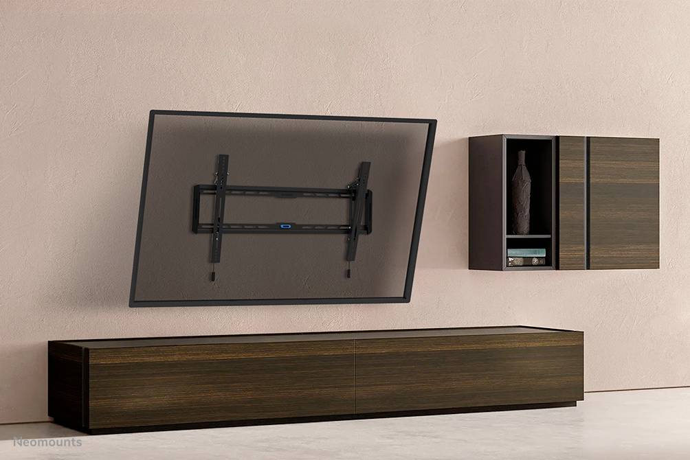 Wandhalterung für einen Fernseher zeigt ein geneigtes TV-Gerät. Unter der Halterung steht ein Holzmöbel. Rechts hängt ein Schrank an der Wand.