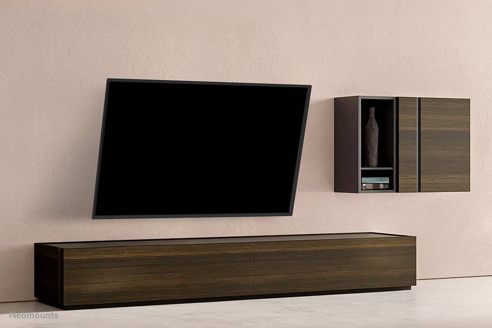 Ein modernes Wohnzimmer-Setup mit einem geneigten Flachbildfernseher an der Wand, daneben ein hölzernes Regal mit Dekoration.