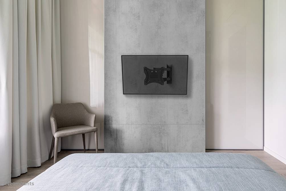 Ein modernes Schlafzimmer mit einem grauen Sessel, einem Bett mit blauem Überwurf und einem an der Wand montierten Fernseher.