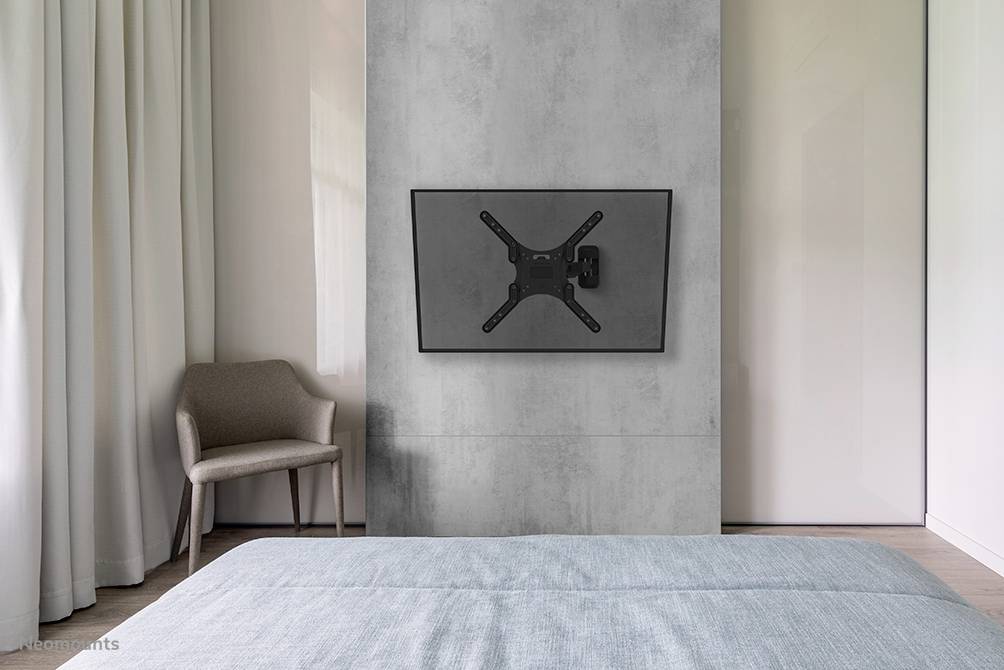 Ein modernes Schlafzimmer zeigt einen an der Wand montierten Flachbildfernseher, einen Stuhl und ein Bett mit blauer Bettdecke.