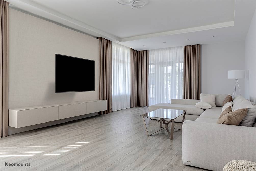Helles Wohnzimmer mit modernem Sofa, Glastisch und großem Flachbildfernseher an der Wand. Große Fenster mit langen Vorhängen.