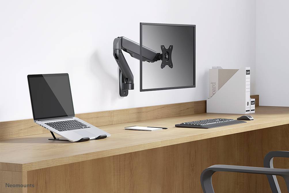 Moderner Arbeitsplatz mit Laptop, Monitor an schwenkbarem Arm, Tastatur und Maus auf einem Holztisch. Aktenordner im Hintergrund.