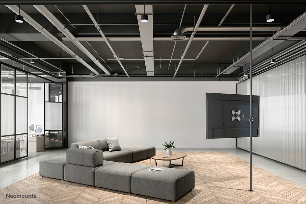 Ein moderner Büroraum mit grauen modularen Sofas auf einem Holzfußboden. An der rechten Wand ist ein großer Bildschirm montiert.