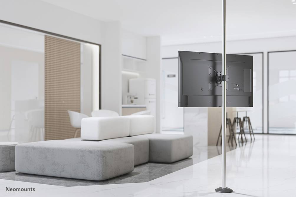 Ein moderner, heller Wohnraum mit einem Flachbildfernseher, der an einer Boden-Decken-Stange montiert ist. Im Hintergrund sind Sofas und eine Küche zu sehen.