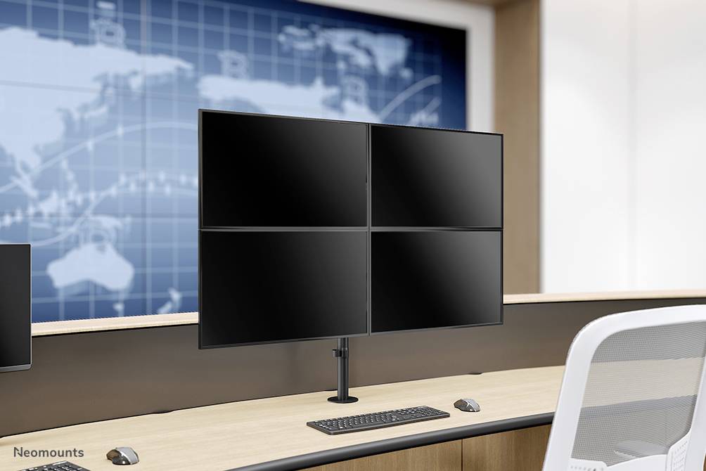 Ein Büro mit einem Schreibtisch, darauf ein Monitorständer mit vier Monitoren. Im Hintergrund ist eine Weltkarte an der Wand zu sehen.