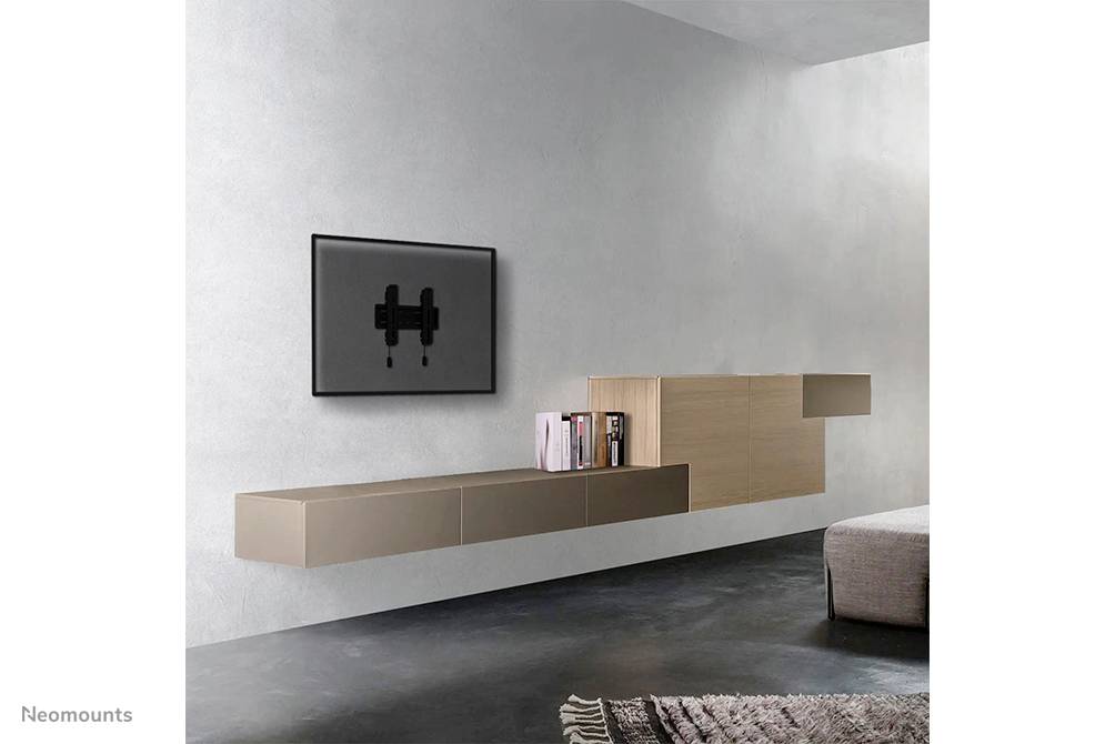 Ein minimalistisches Wohnzimmer mit grauer Wand. Ein flacher Fernseher ist an der Wand montiert, daneben schwebende Regale mit Büchern.