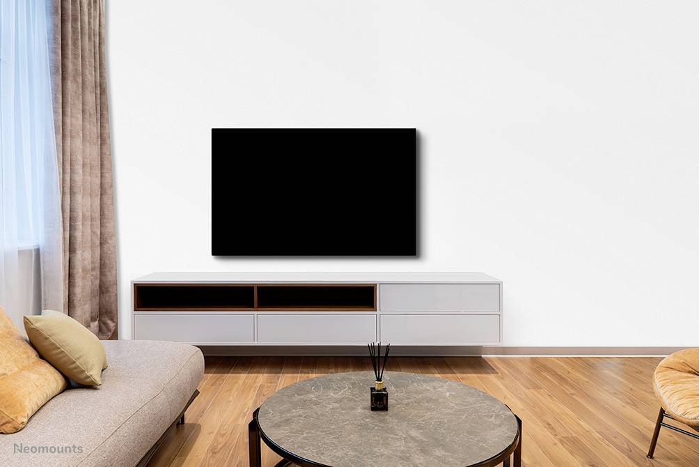 Wohnzimmer mit grauem Sofa, runden Couchtisch und großem, schwarzen Fernseher an weißer Wand. Helles Holzparkett und bodenlanges Fenster mit Vorhang.