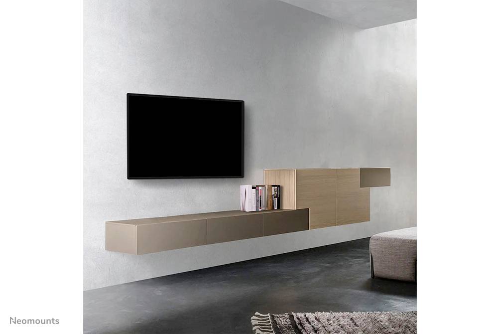 Fernseher an grauer Wand montiert, daneben ein stilvolles Regal mit Büchern. Teppich auf dunklem Boden, modernes Wohnzimmerambiente.