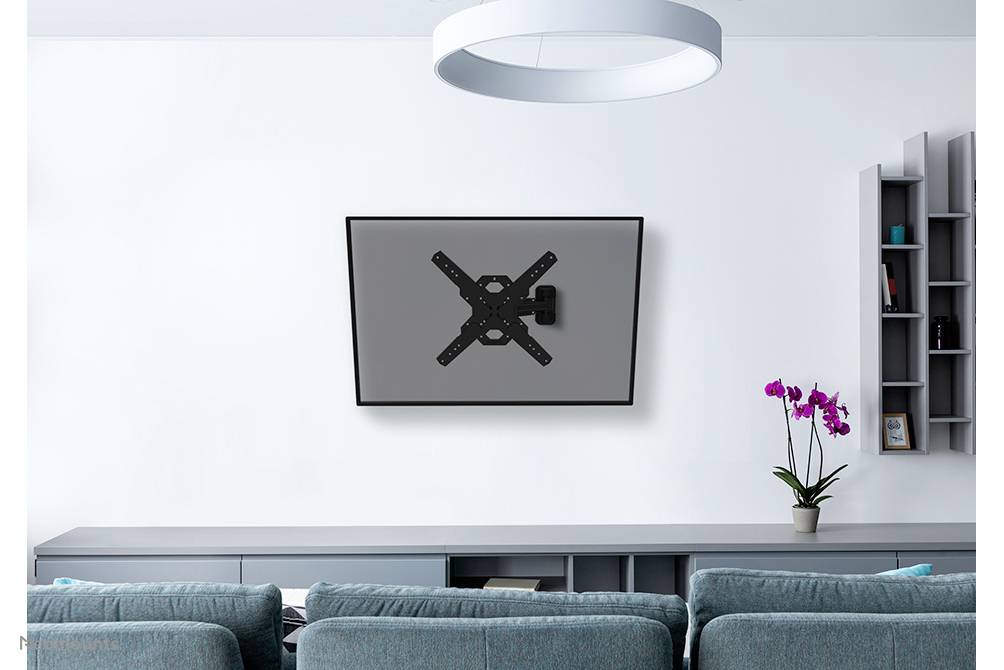 Ein Fernseher an einer Wandhalterung in einem modernen Wohnzimmer mit grauen Möbeln und einem Blumentopf mit Orchideen auf einem Regal.