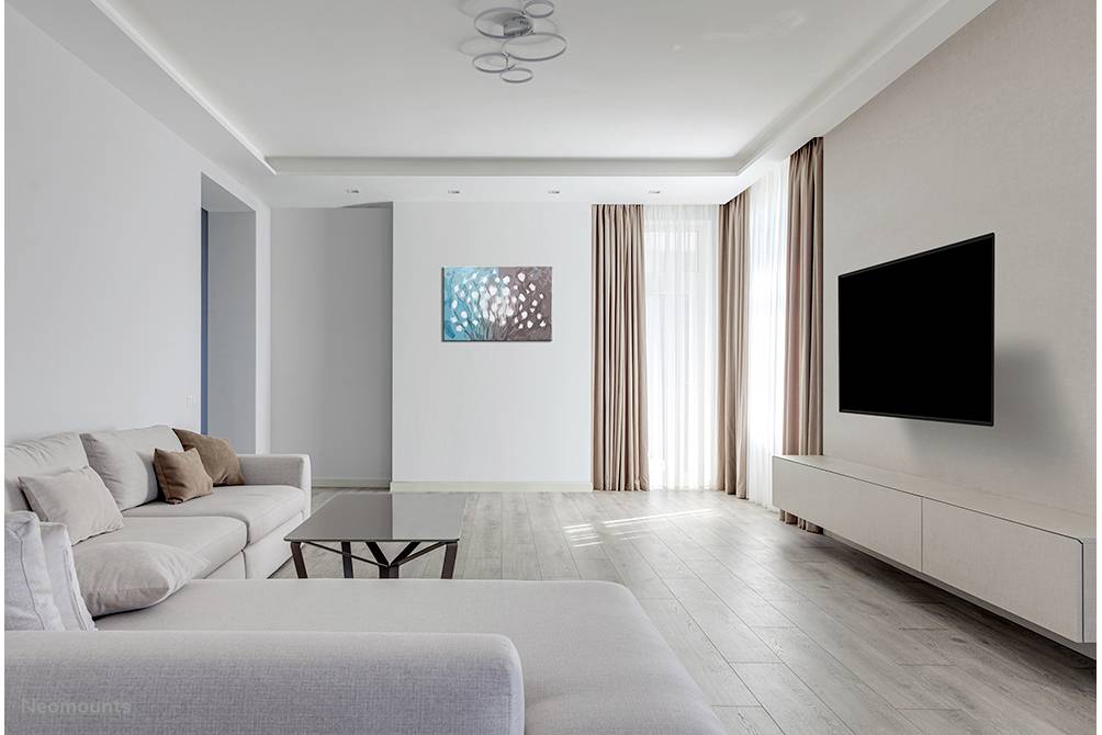 Helles Wohnzimmer mit grauem Sofa, großem schwarzen Flachbildfernseher an der Wand, Holzboden und Tageslicht durch große Fenster.